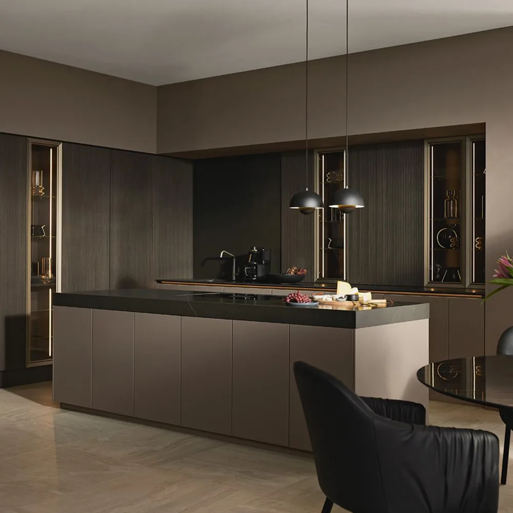 Cocina alemana a medida en tonos topo con isla central, encimera oscura y vitrinas iluminadas en el showroom Per Sé Küchen Pozuelo de Alarcón
