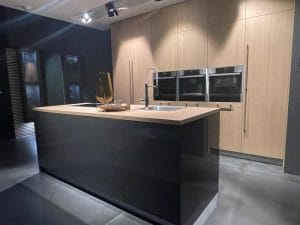 Cocina de diseño alemán con isla central en negro brillante, encimera en madera y columna de armarios con electrodomésticos integrados