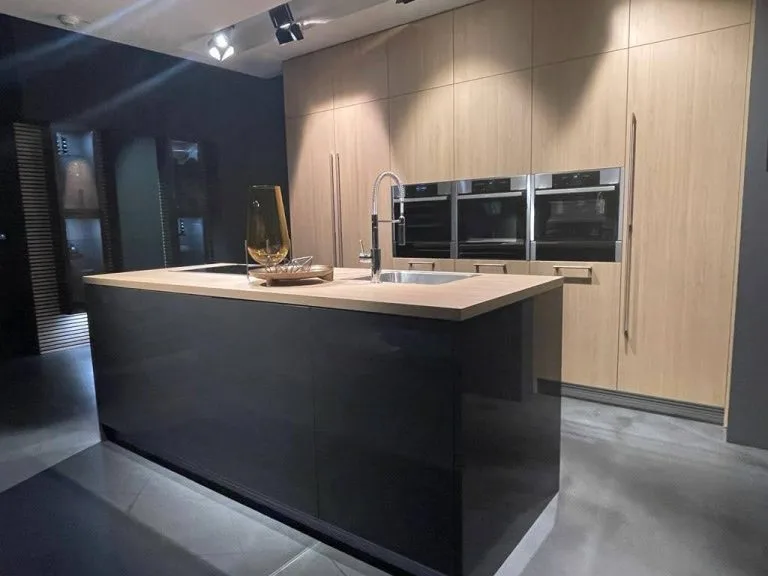 Cocina de diseño alemán con isla central en negro brillante, encimera en madera y columna de armarios con electrodomésticos integrados