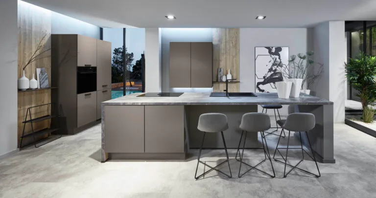 Cocina alemana a medida en gris topo con isla de encimera de mármol, taburetes y vistas a piscina exterior